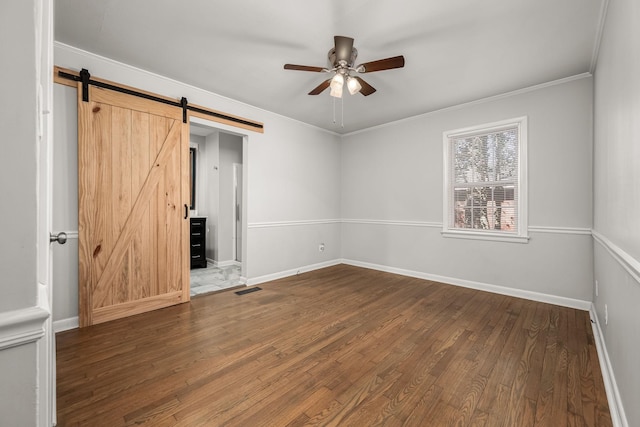 unfurnished bedroom featuring a barn door, baseboards, visible vents, ornamental molding, and wood finished floors