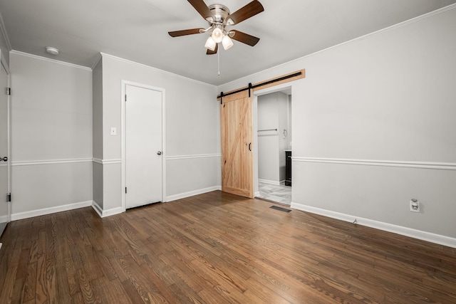 unfurnished bedroom with a barn door, wood finished floors, visible vents, baseboards, and ornamental molding