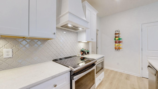 kitchen with light stone counters, tasteful backsplash, custom range hood, appliances with stainless steel finishes, and white cabinetry