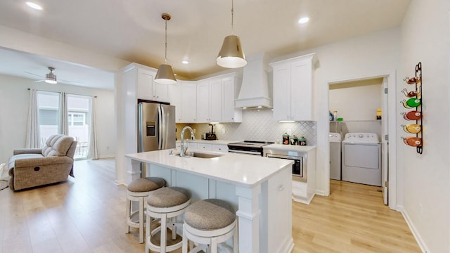 kitchen featuring stainless steel appliances, custom range hood, backsplash, a sink, and separate washer and dryer