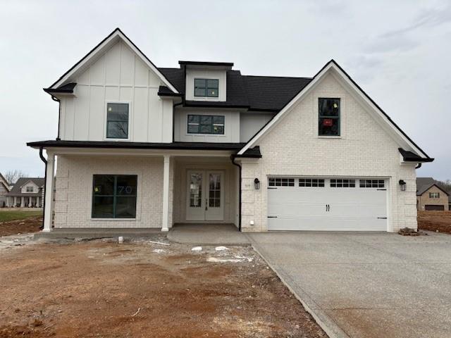 modern farmhouse featuring driveway, an attached garage, french doors, board and batten siding, and brick siding