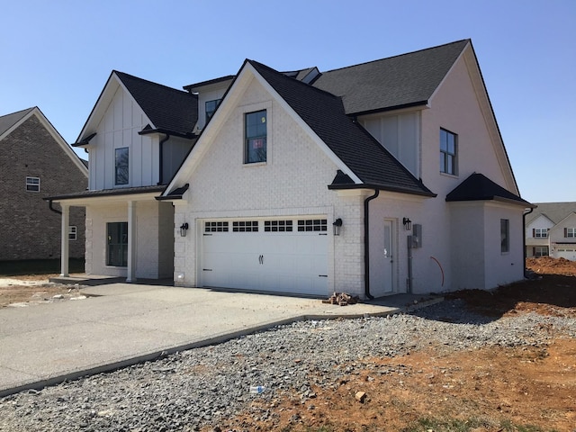 view of front facade featuring brick siding, board and batten siding, roof with shingles, driveway, and an attached garage