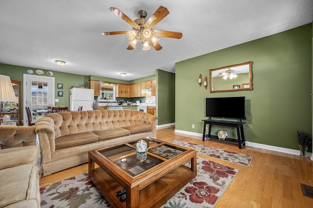 living room featuring baseboards, ceiling fan, a textured ceiling, and light wood finished floors