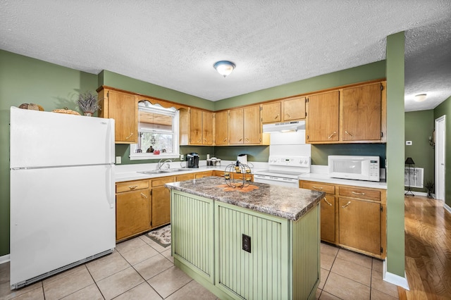 kitchen featuring white appliances, light tile patterned floors, a textured ceiling, under cabinet range hood, and a sink