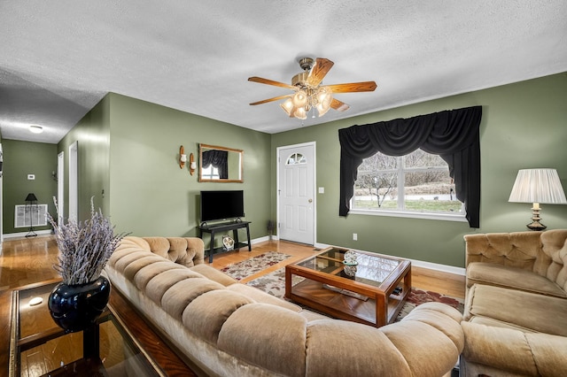 living area featuring a ceiling fan, a textured ceiling, baseboards, and wood finished floors