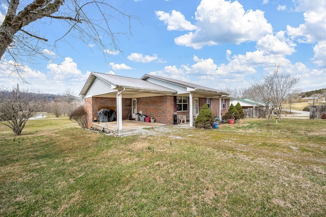 rear view of property with brick siding, a yard, a patio, metal roof, and an attached carport