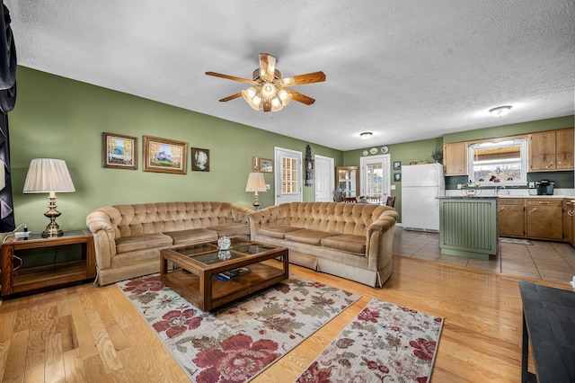 living room with light wood finished floors, a ceiling fan, and a textured ceiling