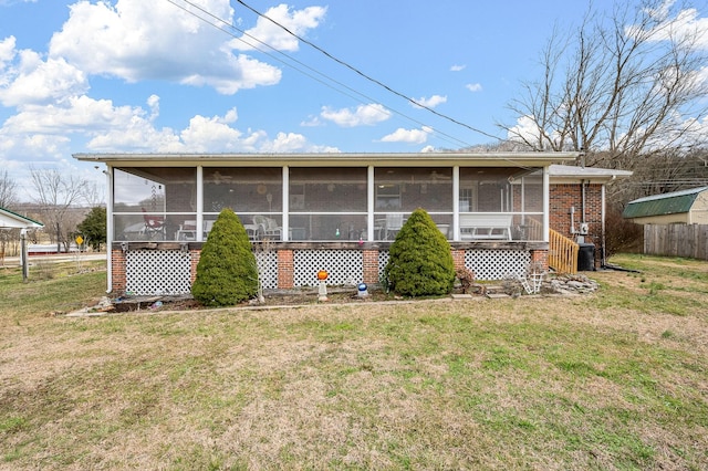 back of house with brick siding, a lawn, fence, and a sunroom