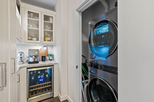 clothes washing area with wine cooler, laundry area, stacked washer / dryer, baseboards, and a bar