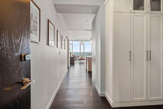 hallway featuring baseboards, a chandelier, and dark wood-type flooring