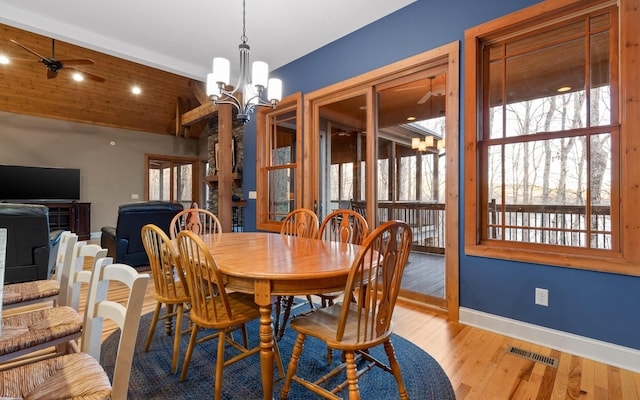 dining space with visible vents, vaulted ceiling, wood finished floors, baseboards, and ceiling fan with notable chandelier