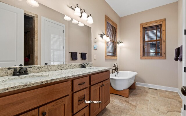 full bathroom featuring stone finish flooring, a freestanding tub, a sink, and baseboards