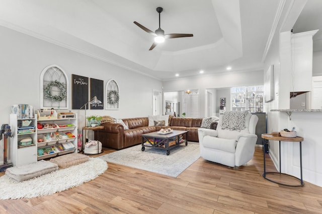 living area featuring light wood-type flooring, a ceiling fan, a tray ceiling, and crown molding