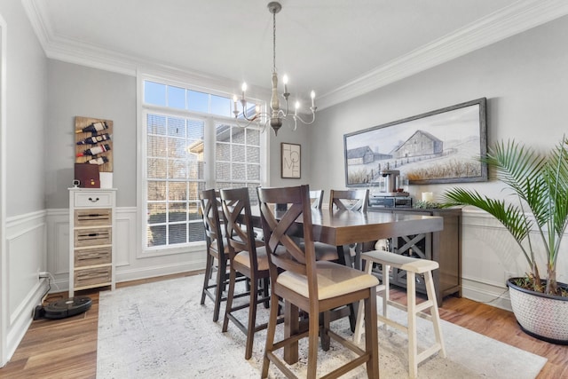 dining room with a notable chandelier, a wainscoted wall, crown molding, and wood finished floors