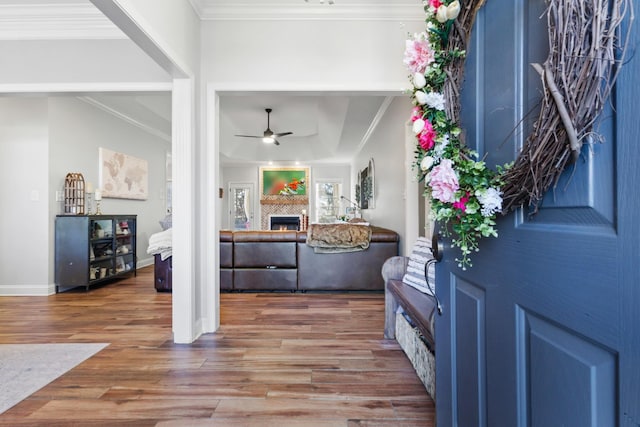 foyer with crown molding, a ceiling fan, wood finished floors, a warm lit fireplace, and baseboards