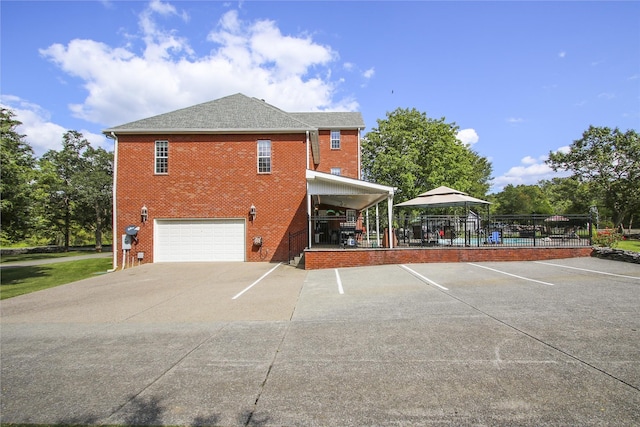 view of property exterior featuring a garage, a gazebo, roof with shingles, and brick siding