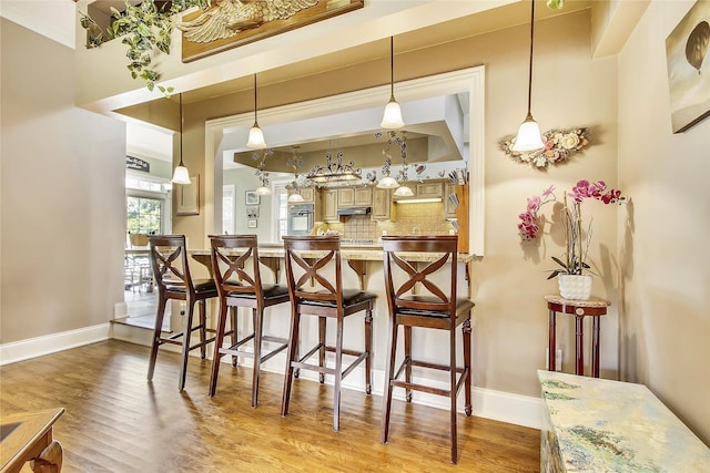 kitchen featuring baseboards, decorative backsplash, a breakfast bar area, wood finished floors, and stainless steel oven