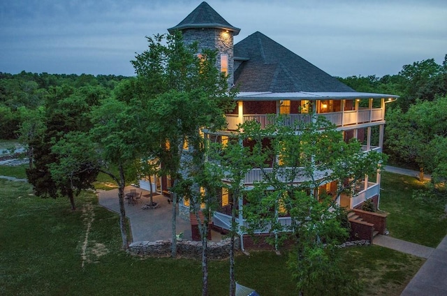 view of side of home featuring a balcony, a patio area, roof with shingles, and a yard