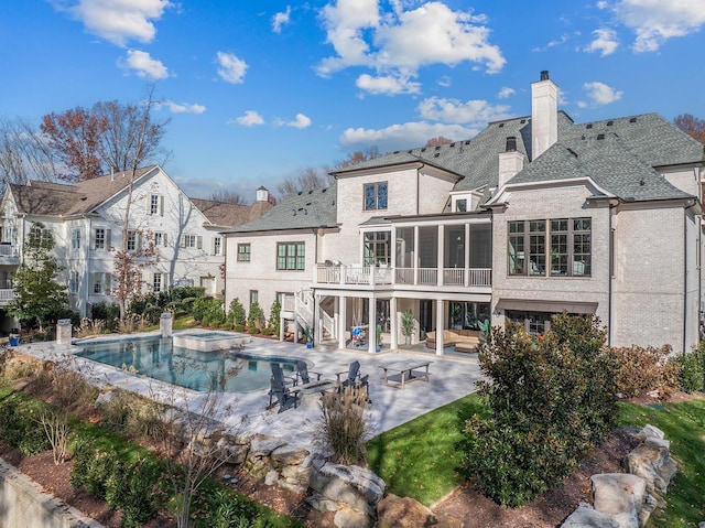 rear view of property with a sunroom, a chimney, stairs, a patio area, and a pool with connected hot tub