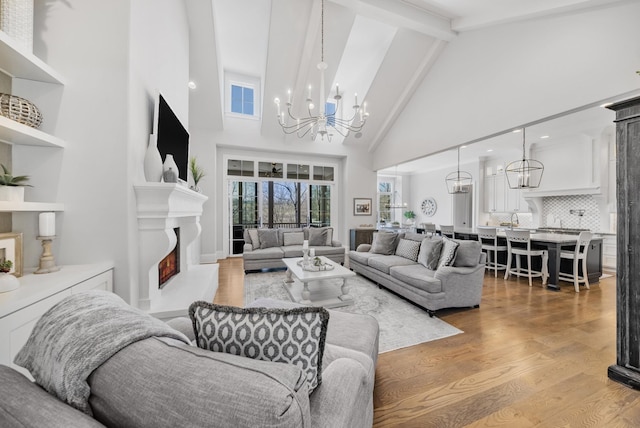 living room with a notable chandelier, a lit fireplace, beamed ceiling, and wood finished floors