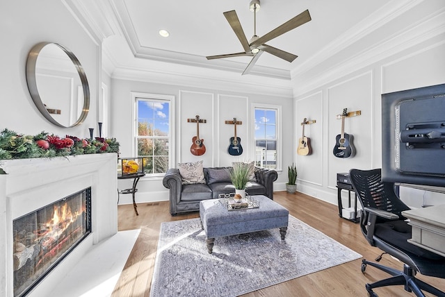 living area featuring a decorative wall, a premium fireplace, ornamental molding, a ceiling fan, and wood finished floors