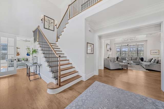 stairway featuring baseboards, a high ceiling, wood finished floors, and crown molding