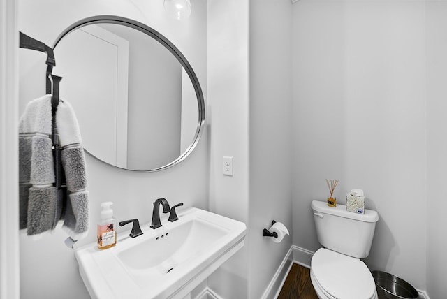 half bath featuring wood finished floors, a sink, toilet, and baseboards