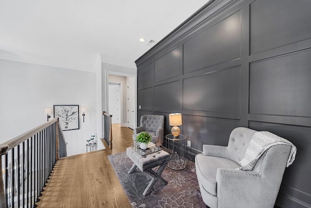 living area featuring a decorative wall, wood finished floors, visible vents, an upstairs landing, and crown molding