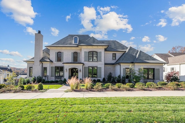 french country style house featuring a chimney and a front yard