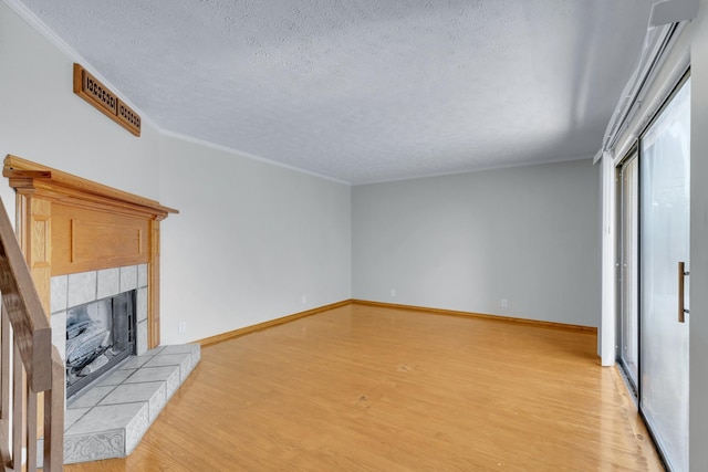 unfurnished living room with baseboards, a tiled fireplace, crown molding, a textured ceiling, and light wood-type flooring