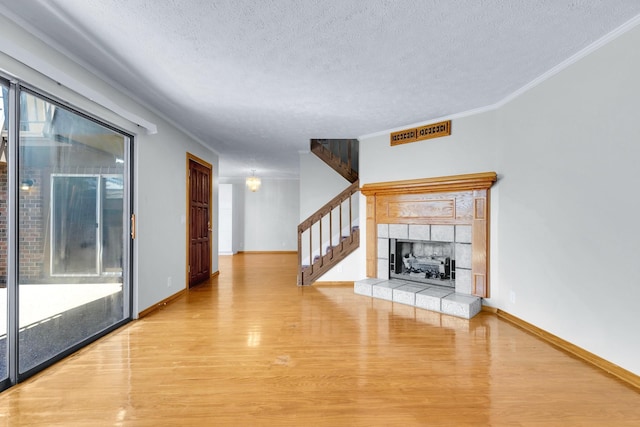 unfurnished living room with a textured ceiling, crown molding, a fireplace, and wood finished floors