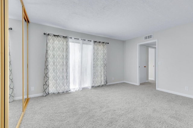 spare room featuring carpet, visible vents, a textured ceiling, and baseboards