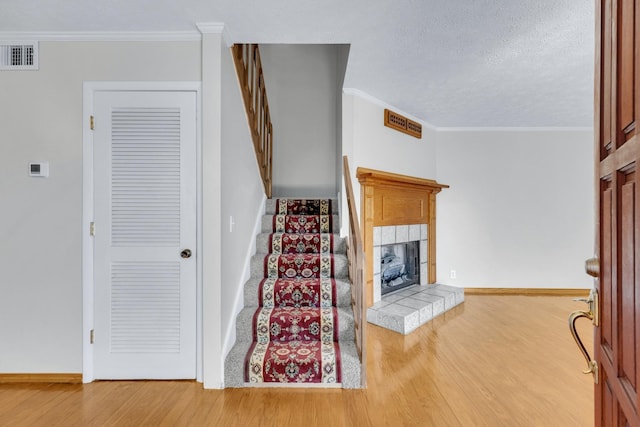 stairs featuring ornamental molding, a tile fireplace, visible vents, and wood finished floors