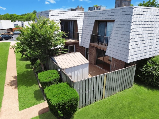 view of property exterior featuring mansard roof, a lawn, a balcony, and brick siding