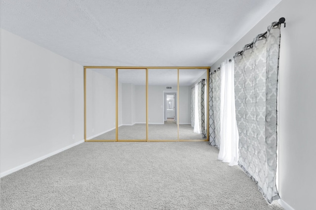 unfurnished bedroom with a textured ceiling, carpet flooring, visible vents, and baseboards