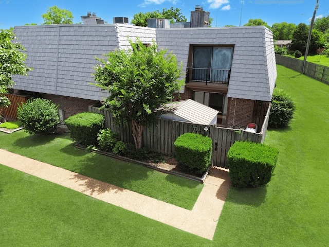 view of front facade with a front yard, fence, mansard roof, and brick siding