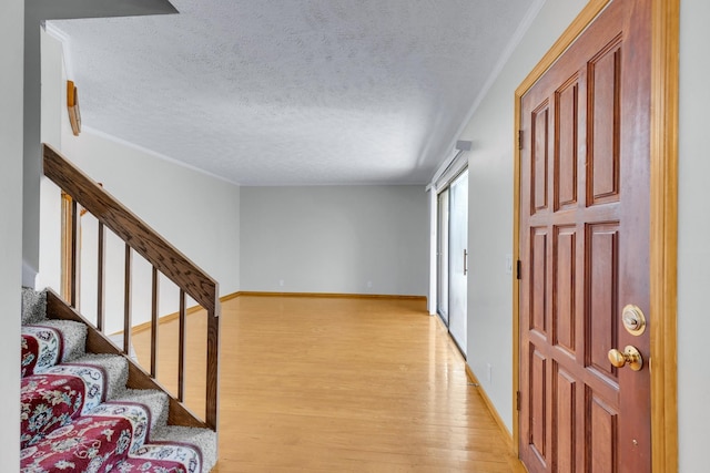 foyer entrance with crown molding, light wood-style flooring, a textured ceiling, baseboards, and stairs