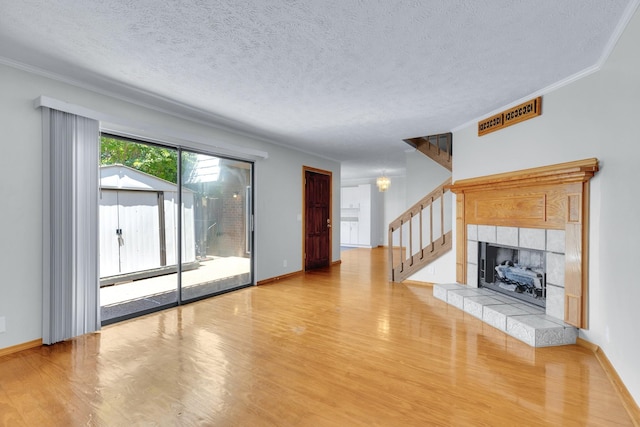 unfurnished living room featuring a fireplace, a textured ceiling, wood finished floors, baseboards, and stairs