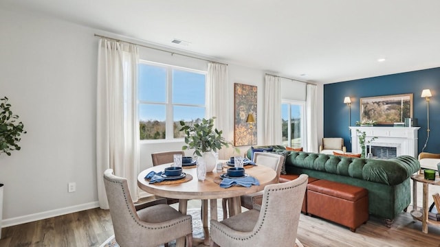 dining room featuring a fireplace, wood finished floors, visible vents, and baseboards