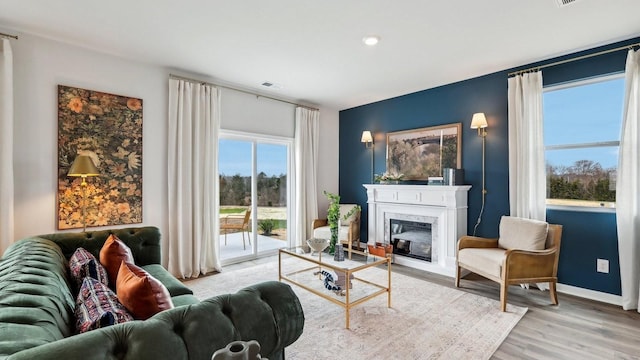 living room with a high end fireplace, visible vents, baseboards, and wood finished floors