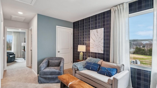 living area featuring a healthy amount of sunlight, an accent wall, baseboards, and carpet flooring