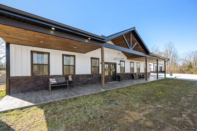 back of property featuring a patio, stone siding, french doors, a lawn, and board and batten siding