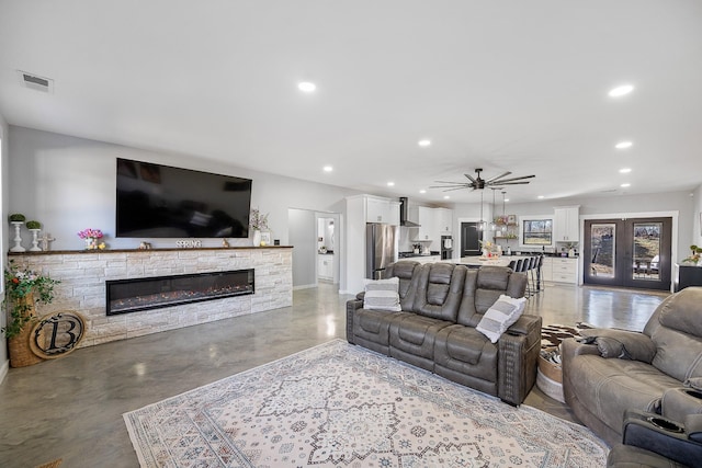 living room featuring visible vents, a ceiling fan, concrete flooring, a stone fireplace, and recessed lighting