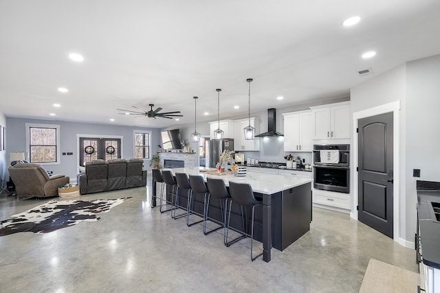 kitchen featuring finished concrete flooring, wall chimney exhaust hood, appliances with stainless steel finishes, and a kitchen breakfast bar