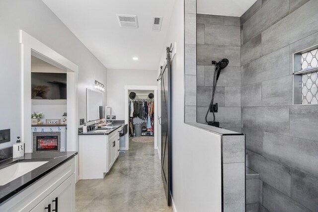 bathroom featuring finished concrete floors, visible vents, walk in shower, and two vanities