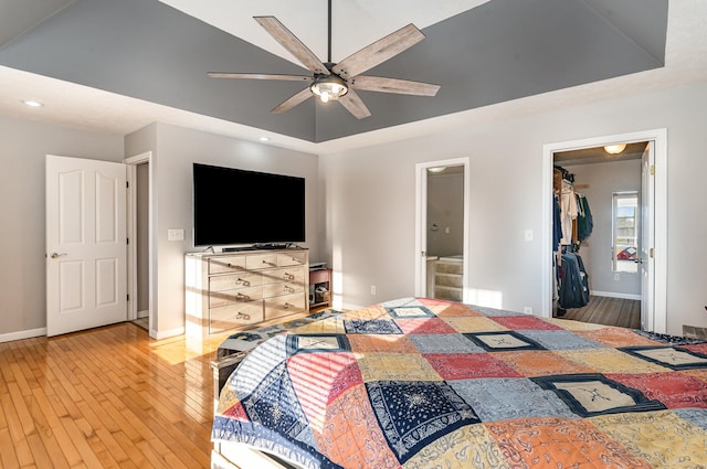 bedroom with a tray ceiling, wood-type flooring, baseboards, and a walk in closet