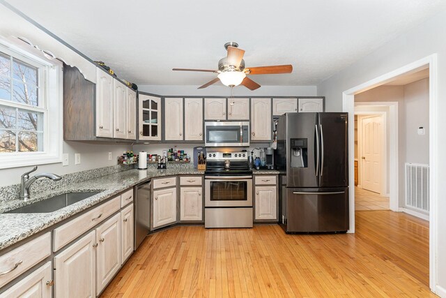 kitchen with visible vents, a sink, stainless steel appliances, light wood-style floors, and light stone countertops