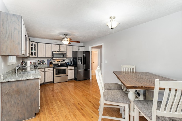 kitchen featuring light wood-style flooring, a sink, stainless steel appliances, glass insert cabinets, and light stone countertops