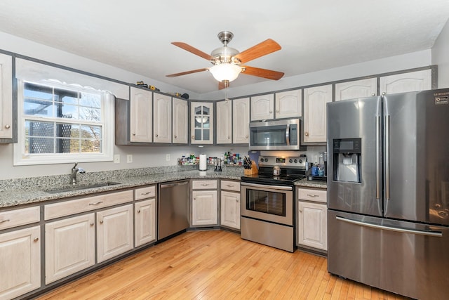 kitchen with light stone counters, a ceiling fan, light wood-style flooring, a sink, and appliances with stainless steel finishes