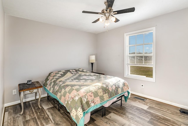 bedroom with ceiling fan, visible vents, baseboards, and wood finished floors